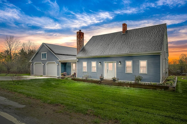 cape cod house featuring a chimney, a yard, an attached garage, and driveway