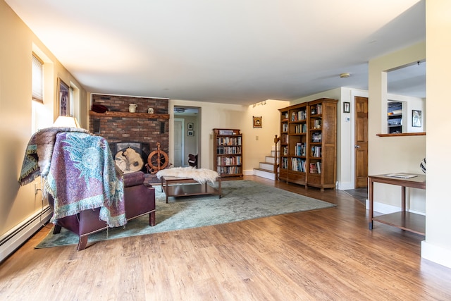 living room featuring a baseboard radiator, wood finished floors, a brick fireplace, and baseboards