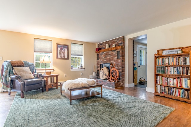 living room with wood finished floors, a brick fireplace, and baseboards