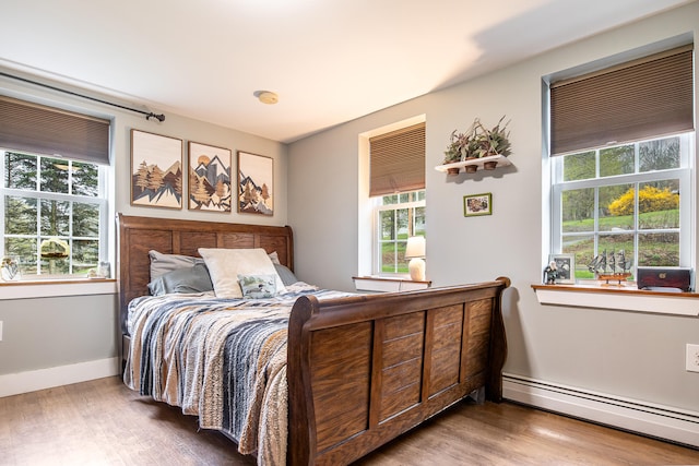 bedroom featuring a baseboard heating unit, wood finished floors, and baseboards