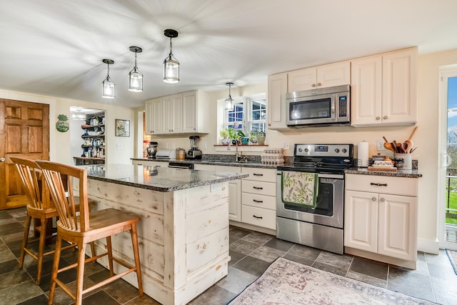 kitchen with stainless steel appliances, a center island, a sink, dark stone counters, and a kitchen bar