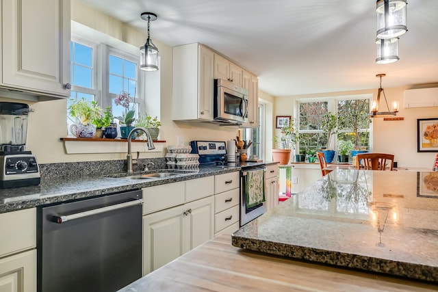 kitchen with appliances with stainless steel finishes, a sink, an AC wall unit, and decorative light fixtures
