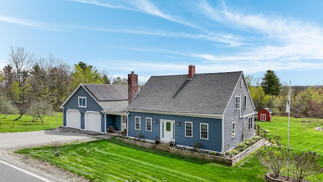 cape cod-style house with driveway, a chimney, a front lawn, solar panels, and a garage