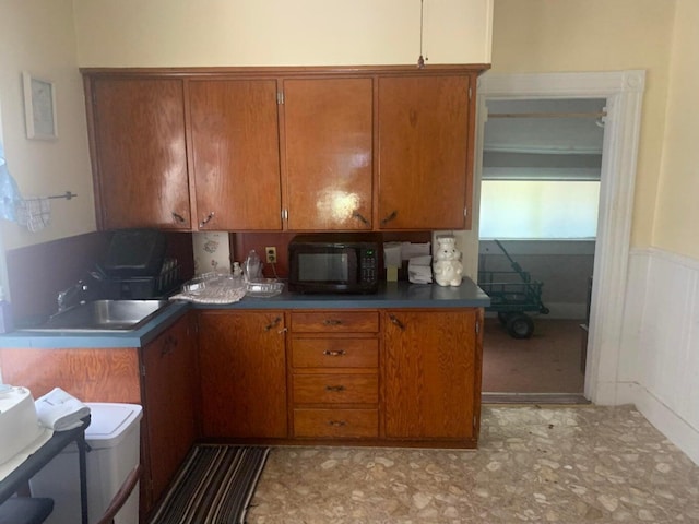 91 Elm St, Millinocket, ME 04462 - kitchen with black microwave, brown cabinetry, a sink, wainscoting, and light flooring