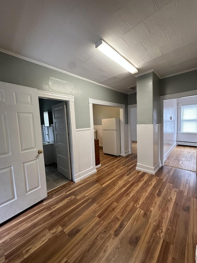 91 Elm St, Millinocket, ME 04462 - below grade area featuring freestanding refrigerator, crown molding, wood finished floors, wainscoting, and a baseboard radiator