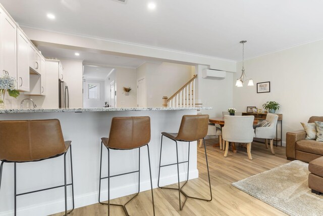 25 Preservation Ln Unit 9, South Portland, ME 04106 - kitchen featuring freestanding refrigerator, light wood finished floors, a breakfast bar, white cabinetry, and crown molding