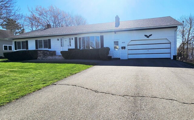 view of front facade featuring a chimney, an attached garage, asphalt driveway, and a front lawn