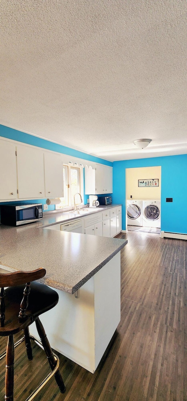 kitchen with separate washer and dryer, stainless steel microwave, a textured ceiling, white cabinets, and a kitchen bar
