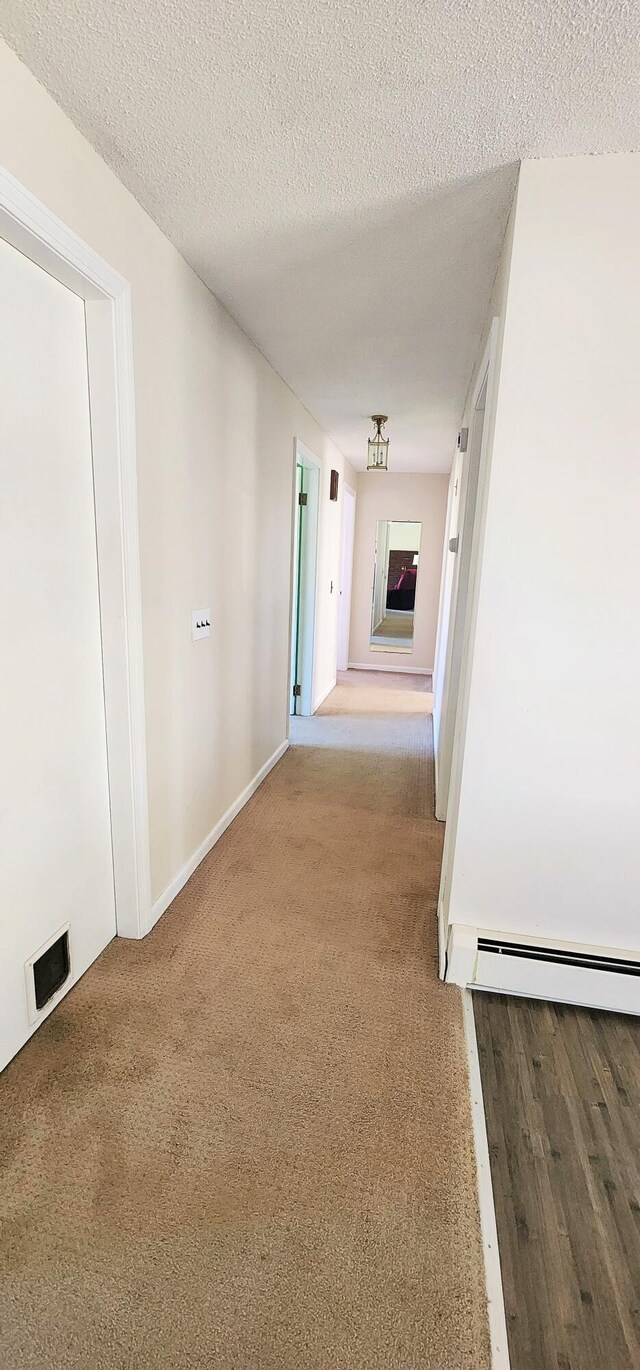 hallway featuring carpet flooring, a textured ceiling, baseboard heating, and baseboards