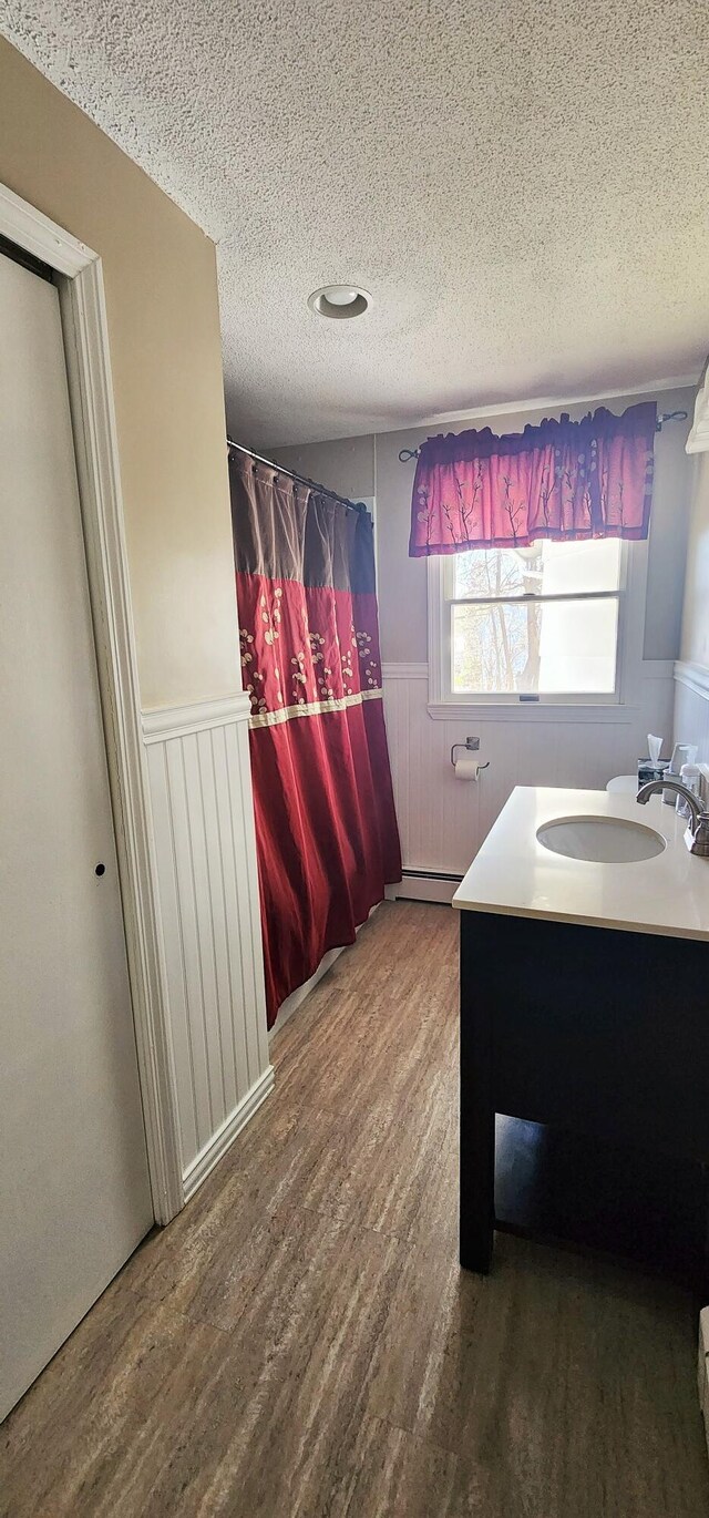 bathroom featuring a wainscoted wall, a textured ceiling, wood finished floors, vanity, and a baseboard heating unit