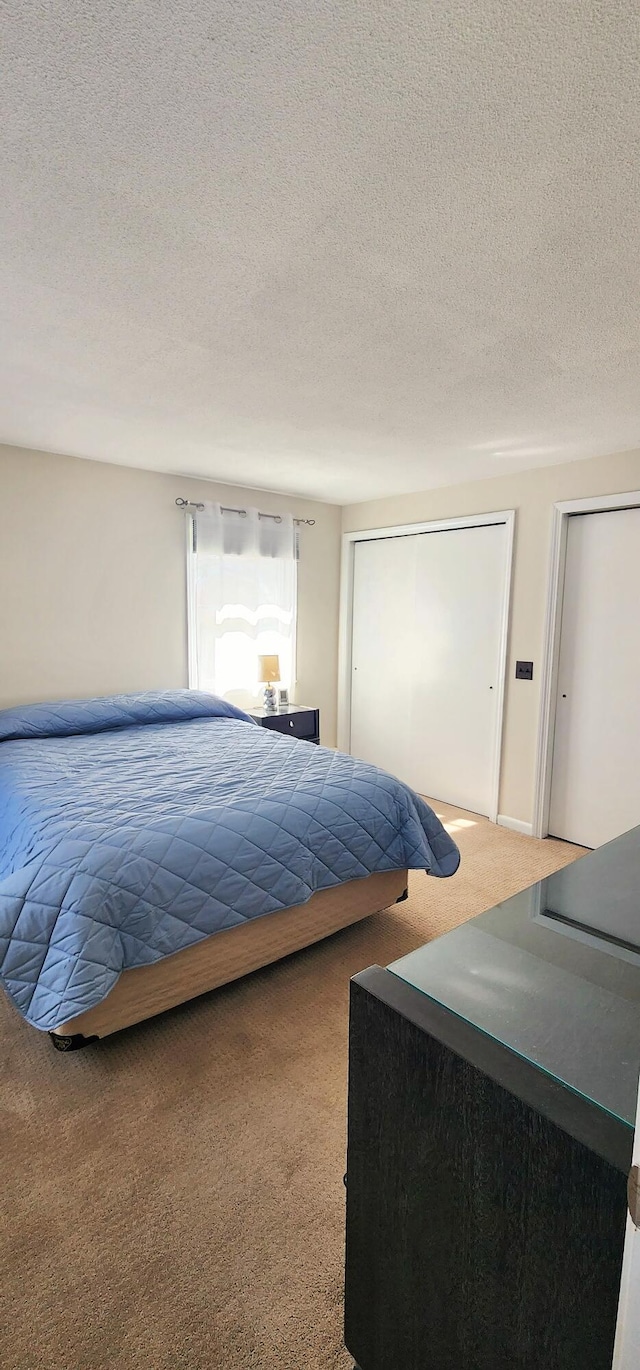 bedroom featuring carpet floors, a textured ceiling, and two closets