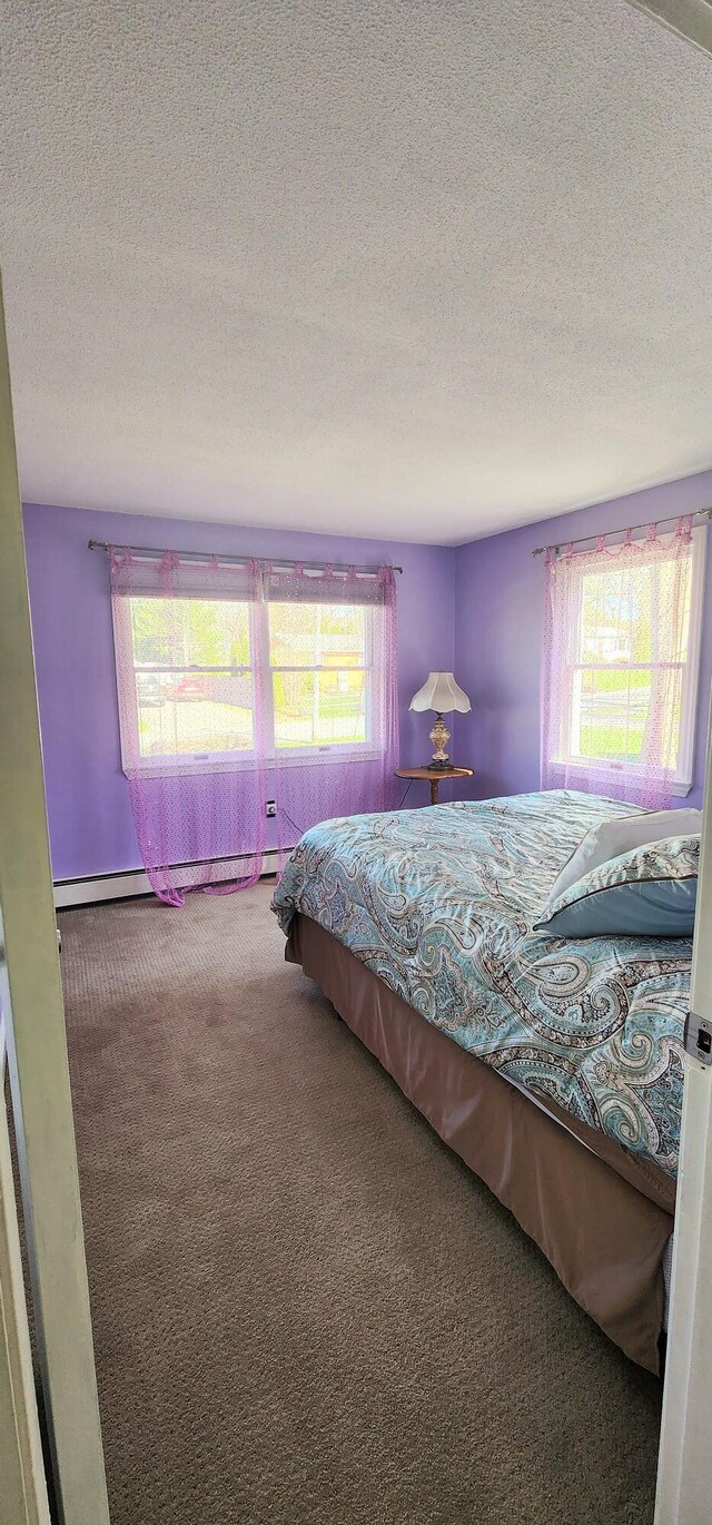 carpeted bedroom featuring a textured ceiling, multiple windows, and a baseboard heating unit
