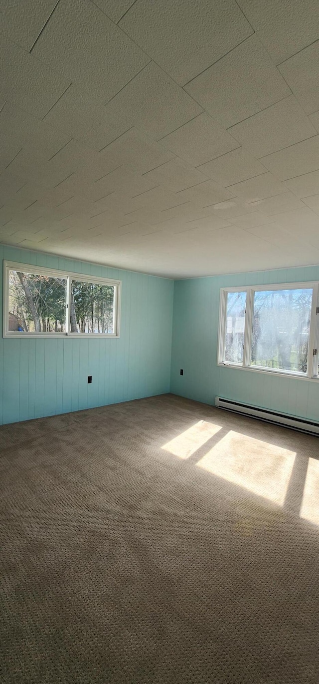 unfurnished room featuring healthy amount of natural light, a baseboard heating unit, and carpet floors