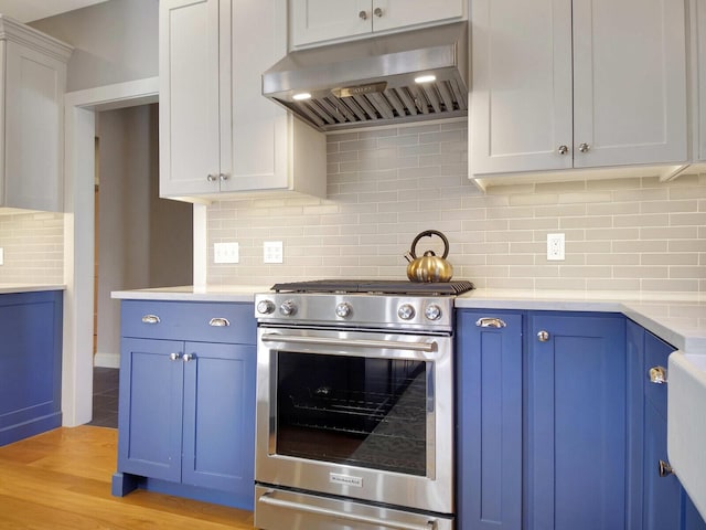 kitchen with high end stove, under cabinet range hood, blue cabinets, light countertops, and backsplash