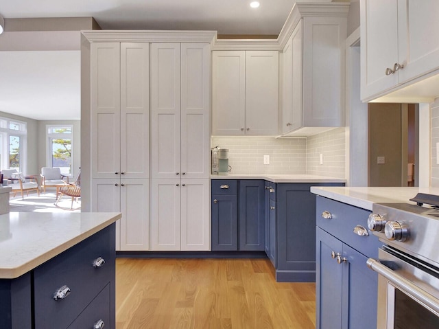 kitchen with blue cabinetry, stainless steel range, light countertops, light wood-type flooring, and white cabinets