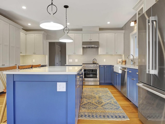 kitchen with stainless steel appliances, blue cabinetry, a sink, under cabinet range hood, and light countertops