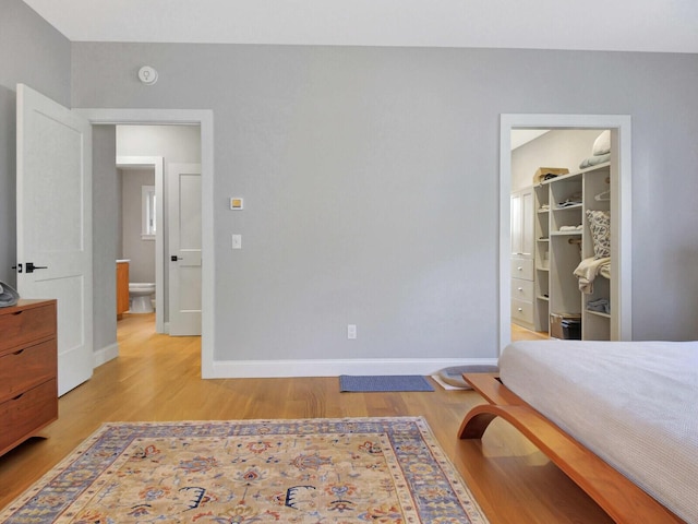 bedroom featuring a spacious closet, light wood-type flooring, baseboards, and a closet