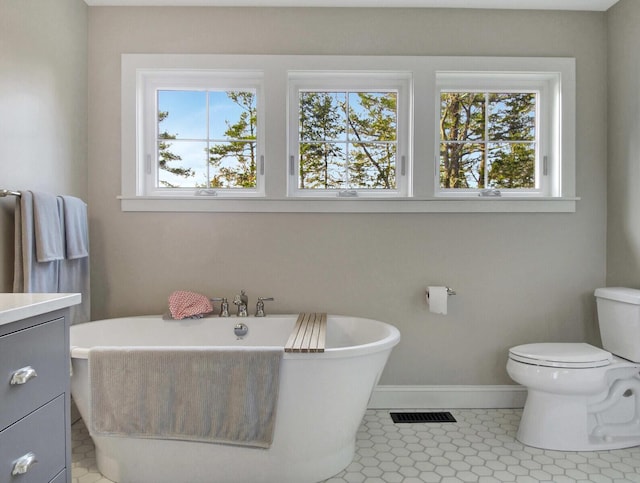 full bath with baseboards, toilet, a freestanding tub, vanity, and tile patterned flooring