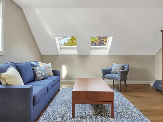living area featuring a skylight, wood finished floors, lofted ceiling, and baseboards