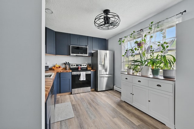 kitchen with appliances with stainless steel finishes, a textured ceiling, light wood-type flooring, wood counters, and baseboard heating