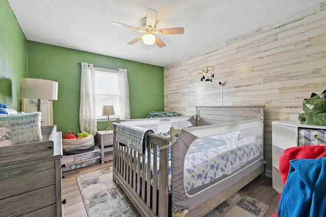 bedroom featuring wooden walls, a textured ceiling, wood finished floors, and a ceiling fan