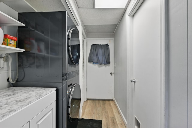 laundry room featuring estacked washer and dryer, light wood-type flooring, and baseboards