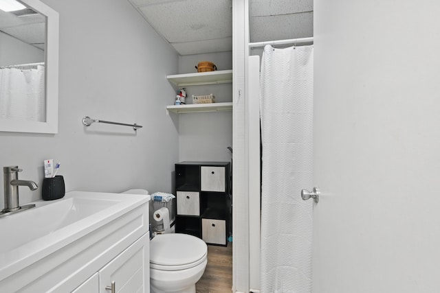 bathroom featuring toilet, a drop ceiling, wood finished floors, a shower with shower curtain, and vanity