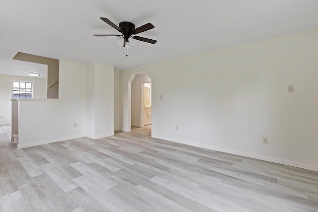 spare room featuring ceiling fan, arched walkways, light wood-type flooring, and baseboards