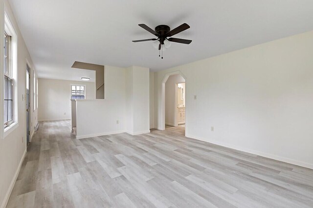 empty room featuring ceiling fan, light wood-style floors, arched walkways, and baseboards