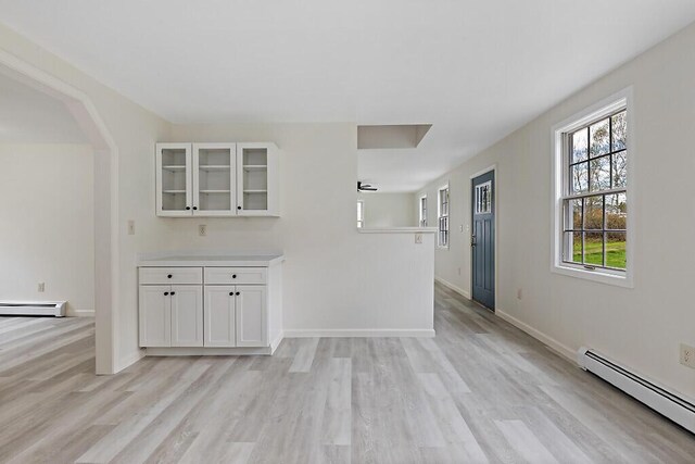 unfurnished living room featuring baseboard heating, light wood-style flooring, a baseboard radiator, arched walkways, and baseboards