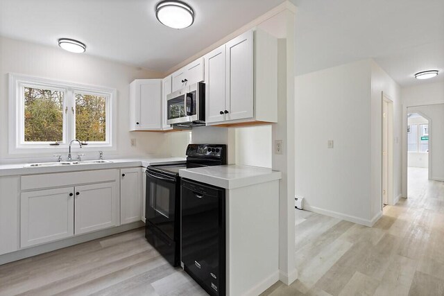 kitchen featuring stainless steel microwave, black electric range, a sink, light wood-style flooring, and light countertops
