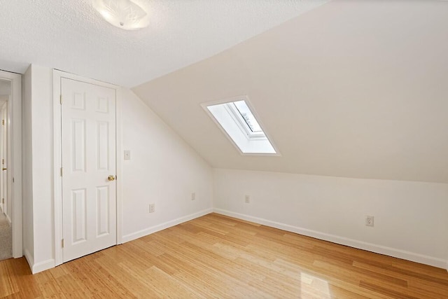 additional living space with a skylight, light wood finished floors, baseboards, and vaulted ceiling