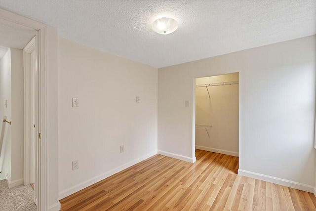 spare room featuring a textured ceiling, light wood-type flooring, and baseboards