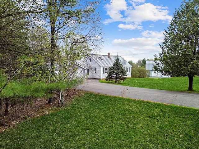 view of front of property featuring asphalt driveway, a chimney, and a front lawn