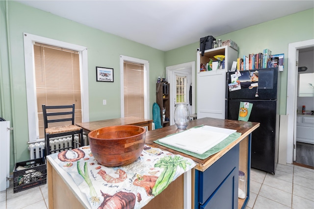 kitchen featuring freestanding refrigerator, light tile patterned flooring, blue cabinetry, and radiator heating unit