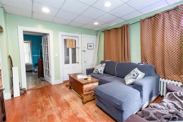 living area featuring radiator, light wood-style flooring, a paneled ceiling, baseboards, and recessed lighting