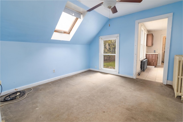 additional living space featuring radiator heating unit, lofted ceiling, light carpet, ceiling fan, and a skylight