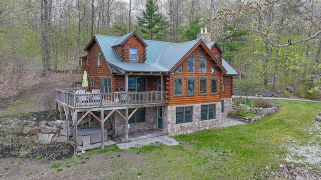 back of house with log exterior, a chimney, stone siding, a yard, and a deck