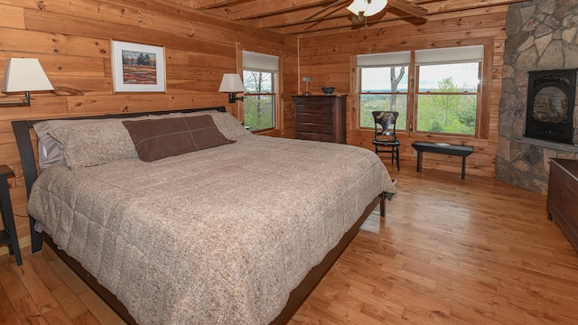 bedroom with hardwood / wood-style floors, wooden walls, beamed ceiling, and a stone fireplace