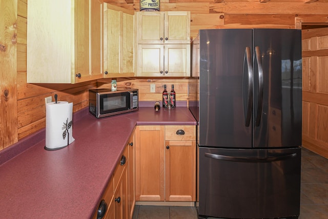 kitchen with freestanding refrigerator, stainless steel microwave, wood walls, dark countertops, and dark tile patterned floors
