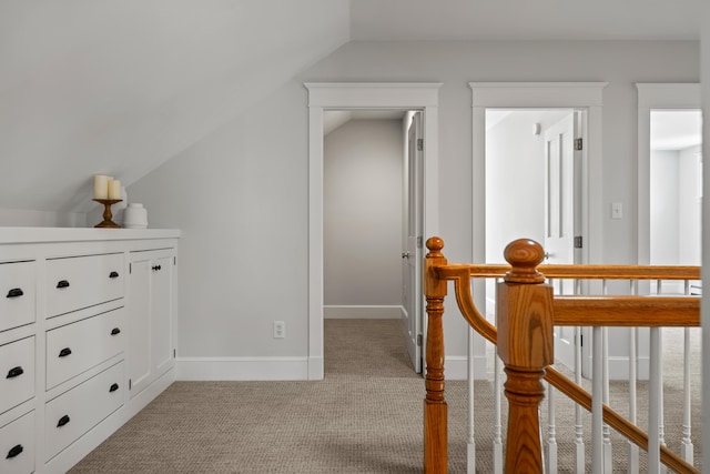 hallway with vaulted ceiling, light carpet, baseboards, and an upstairs landing