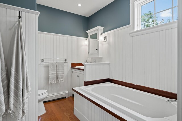 bathroom featuring a baseboard radiator, a bath, a wainscoted wall, toilet, and vanity