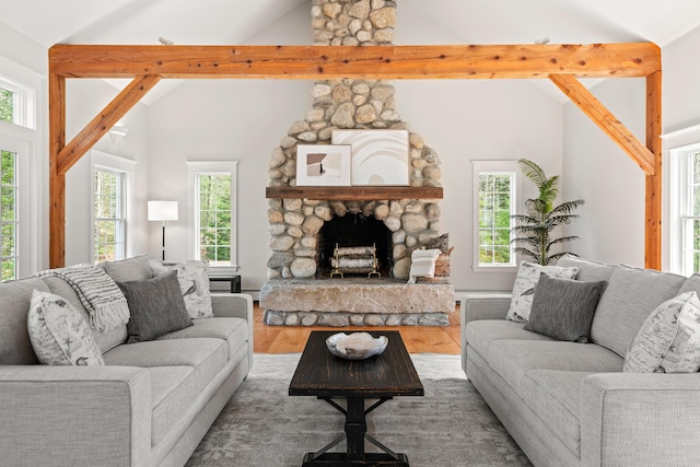 living area with wood finished floors, healthy amount of natural light, high vaulted ceiling, a stone fireplace, and beamed ceiling