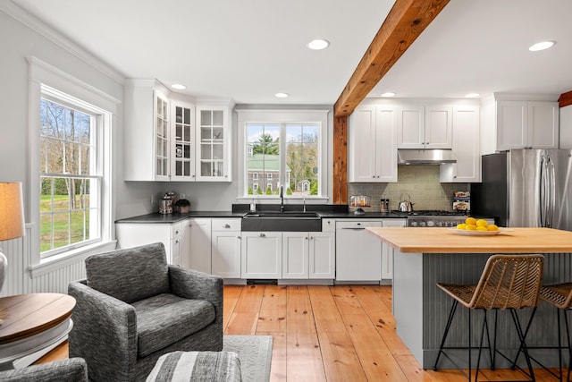 kitchen with a sink, stainless steel appliances, under cabinet range hood, a kitchen breakfast bar, and white cabinetry