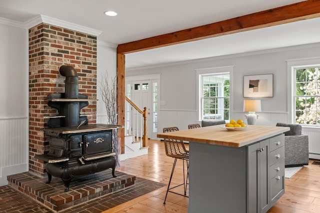 kitchen featuring gray cabinetry, a wood stove, butcher block countertops, a kitchen breakfast bar, and ornamental molding