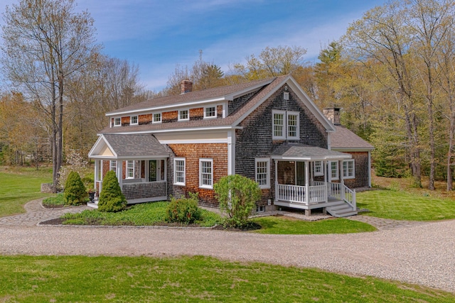 shingle-style home featuring a chimney, a front lawn, and a shingled roof