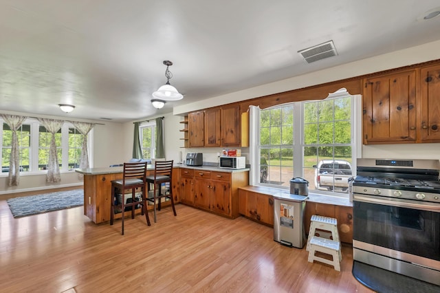 28-30 W Winds Dr, Lebanon, ME 04027 - kitchen with stainless steel gas stove, a peninsula, brown cabinets, light countertops, and light wood-style floors