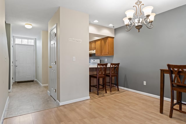 kitchen featuring a chandelier, under cabinet range hood, baseboards, a kitchen breakfast bar, and brown cabinetry