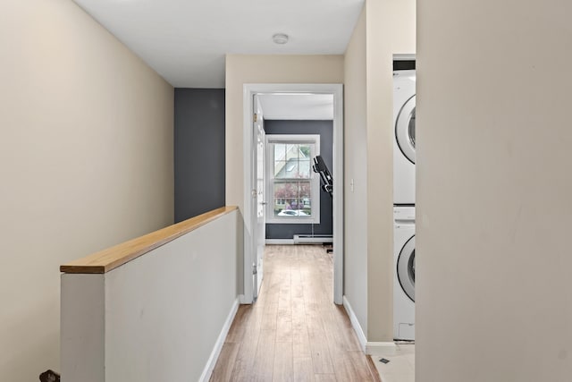 laundry room featuring stacked washing machine and dryer, light wood-type flooring, a baseboard radiator, and baseboards