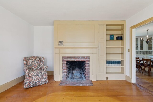 538 Malbons Mills Rd, Skowhegan, ME 04976 - living room with wood finished floors, built in shelves, a brick fireplace, a chandelier, and baseboards